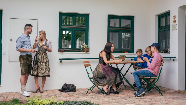 People in traditional dress on a vineyard, some standing, others sitting at a table.