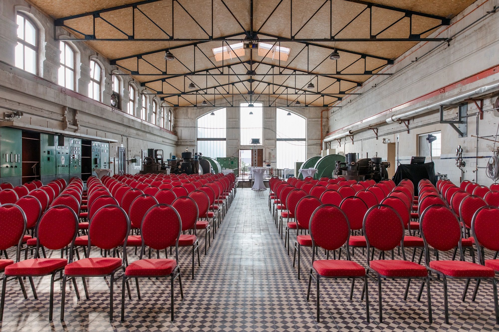 Interior view of an old turbine hall with red chairs and industrial machines.