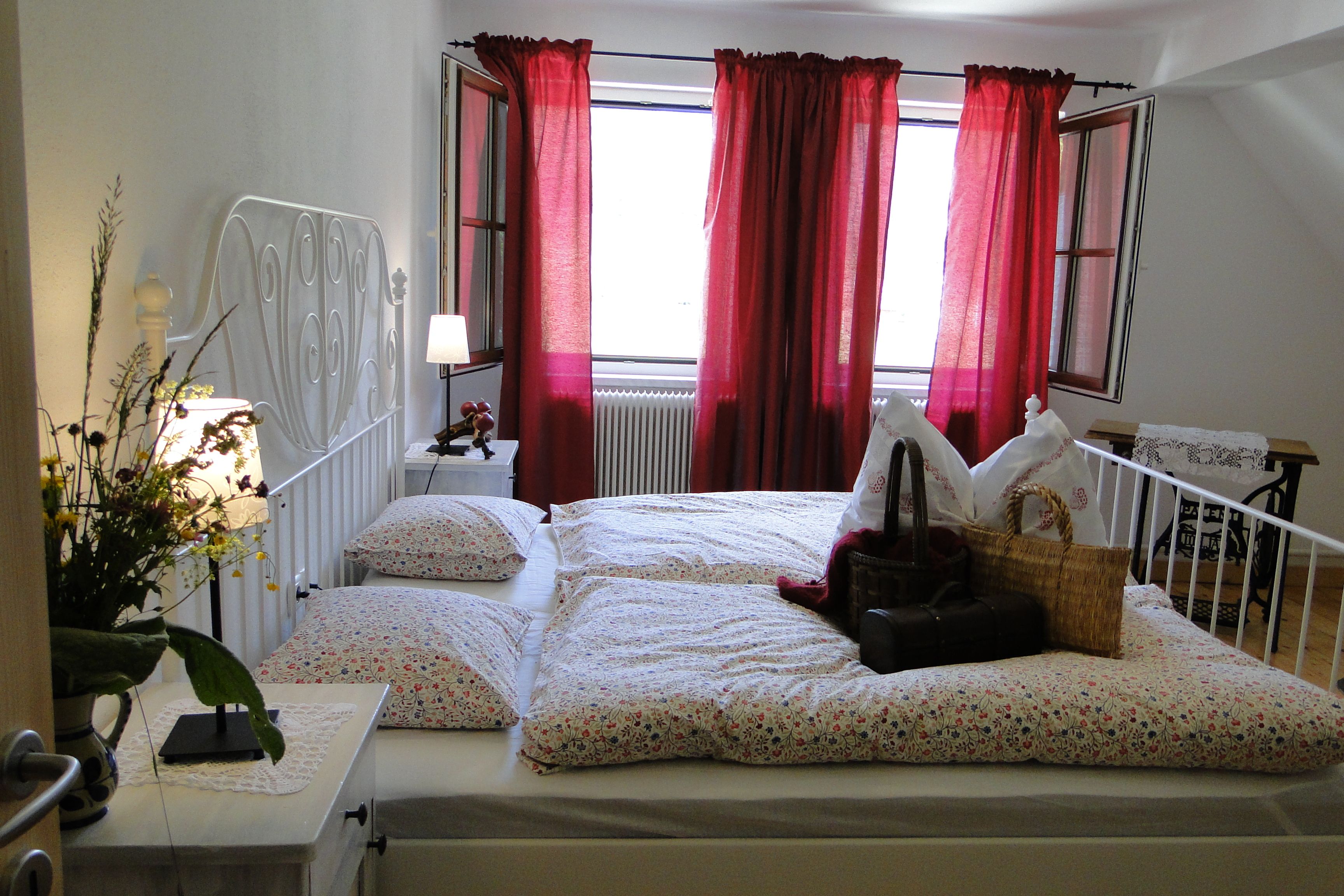 Cozy bedroom with double bed, red curtains and flowers on the bedside table.