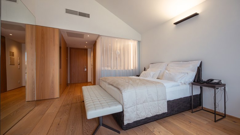 Modern hotel room with large bed, wooden floor and minimalist furnishings.