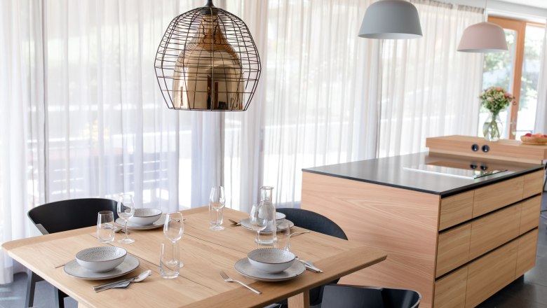 Modern kitchen with wooden table, set for four people, and kitchen island in the background.