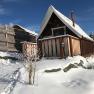 A snow-covered wooden hut with a pointed roof and veranda in a wintry landscape.