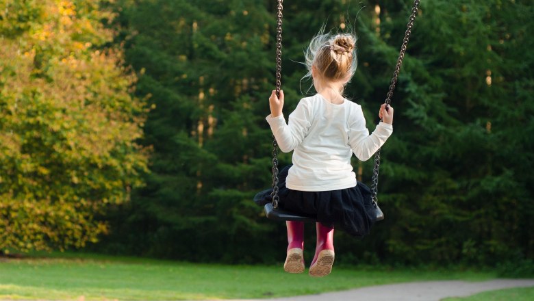 A child swings in a park surrounded by green trees.