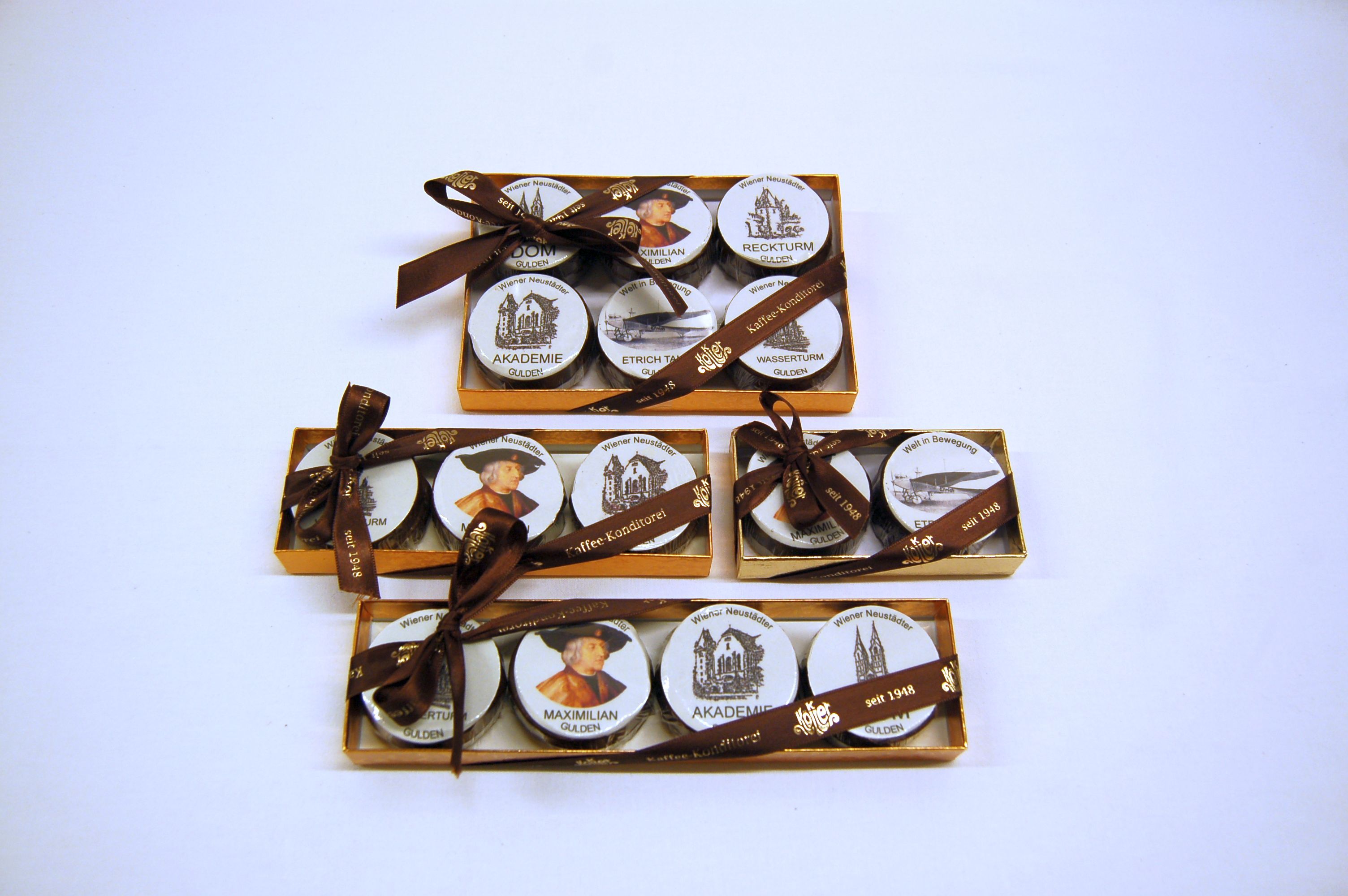 Three golden boxes with round, printed sweets, decorated with brown bows.