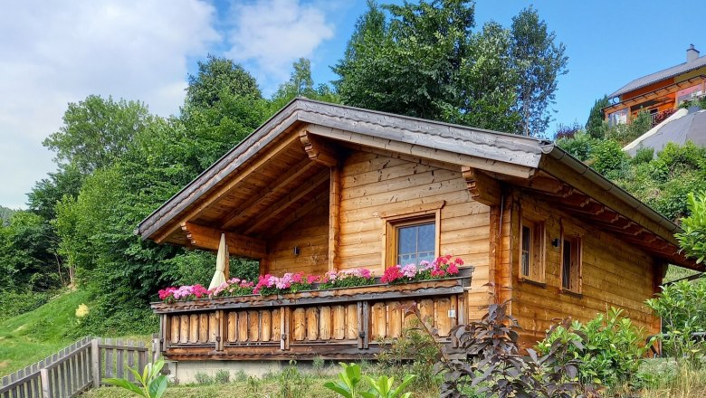 The little paradise, © Fam. Auer Wooden hut with flowers on the veranda in a green setting.