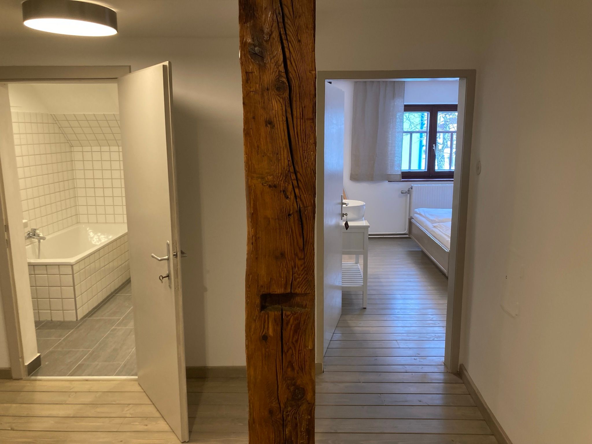 One bathroom and one bedroom with wooden floor, separated by a wooden beam wall.