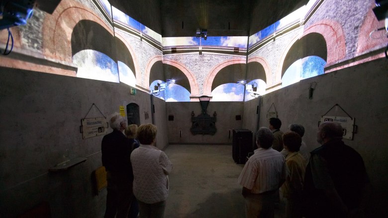 People watch a multimedia show in a room with projections of arches on the walls.