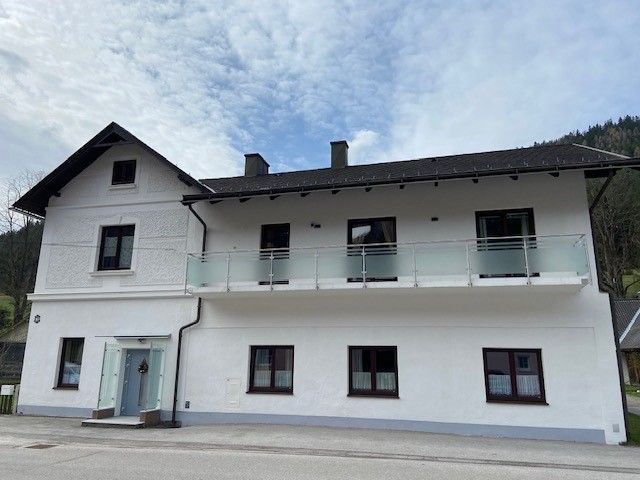 Two-story white house with balcony and blue sky in the background.