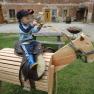A child sits on a wooden toy horse outdoors.