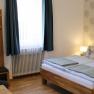 Comfortable double room with bed, closet, table, chair and window with blue curtains.