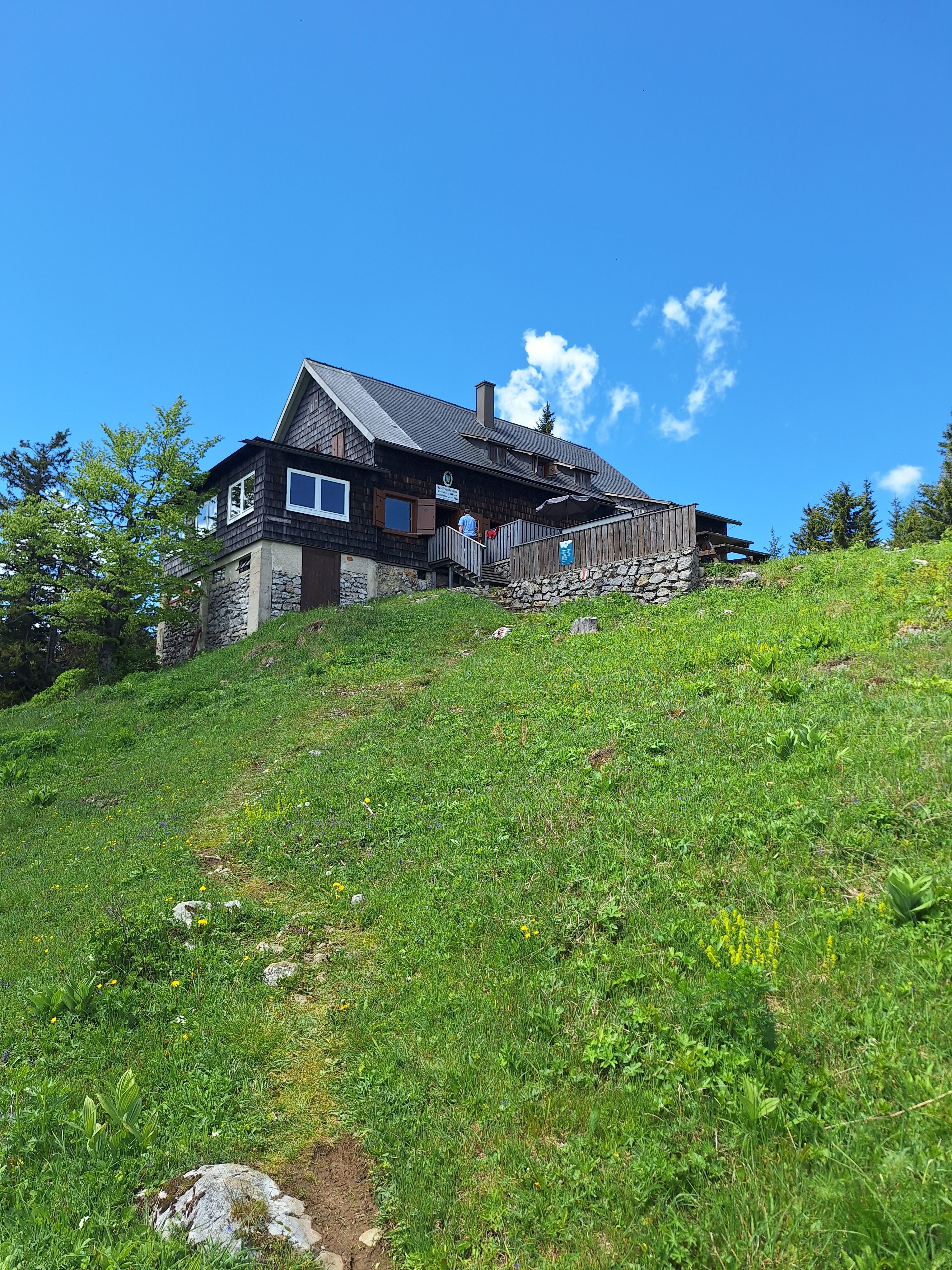 A mountain hut on a green meadow under a blue sky.