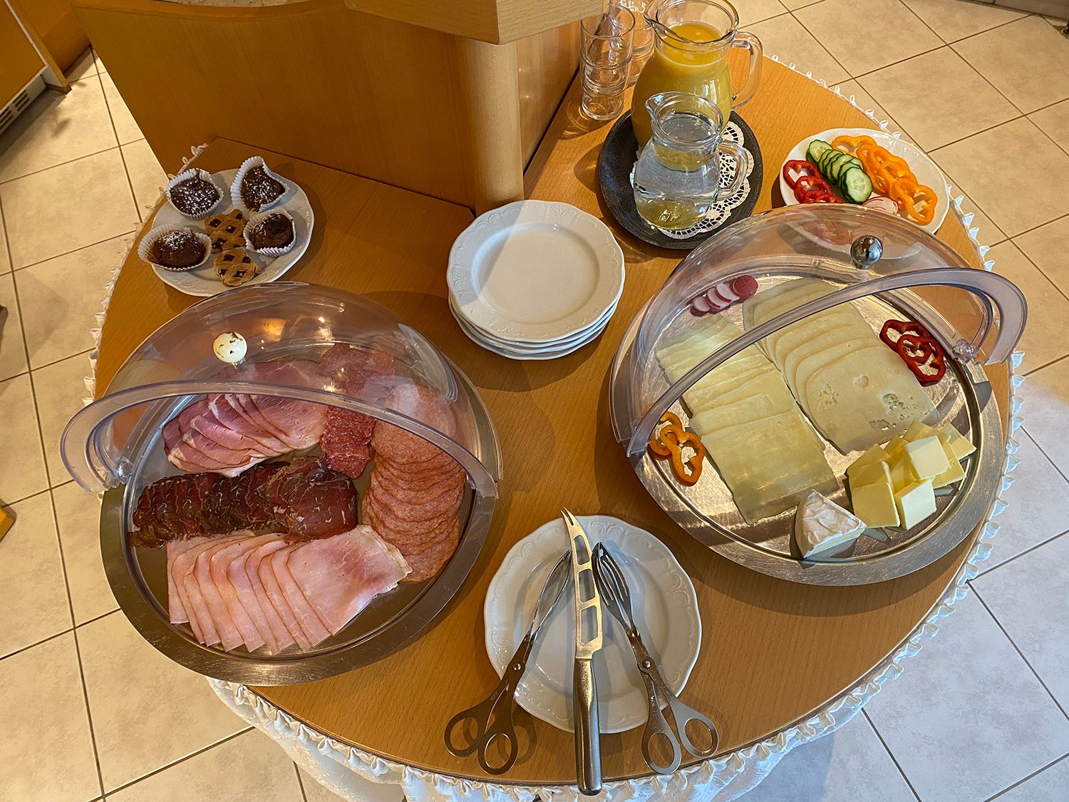 A breakfast buffet with cold cuts, cheese, vegetables, pastries and drinks on a table.