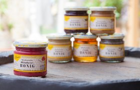 Various jars of honey on a table, raspberry honey in the foreground.