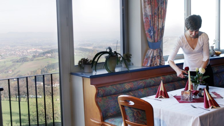 A woman sets a table in a restaurant with a view of a rural landscape.