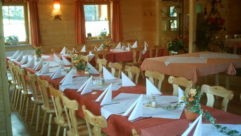 A rustic dining room with wooden furniture, laid tables and decorative flower arrangements.