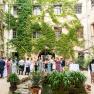 People gather in a leafy courtyard with tables and decorations.
