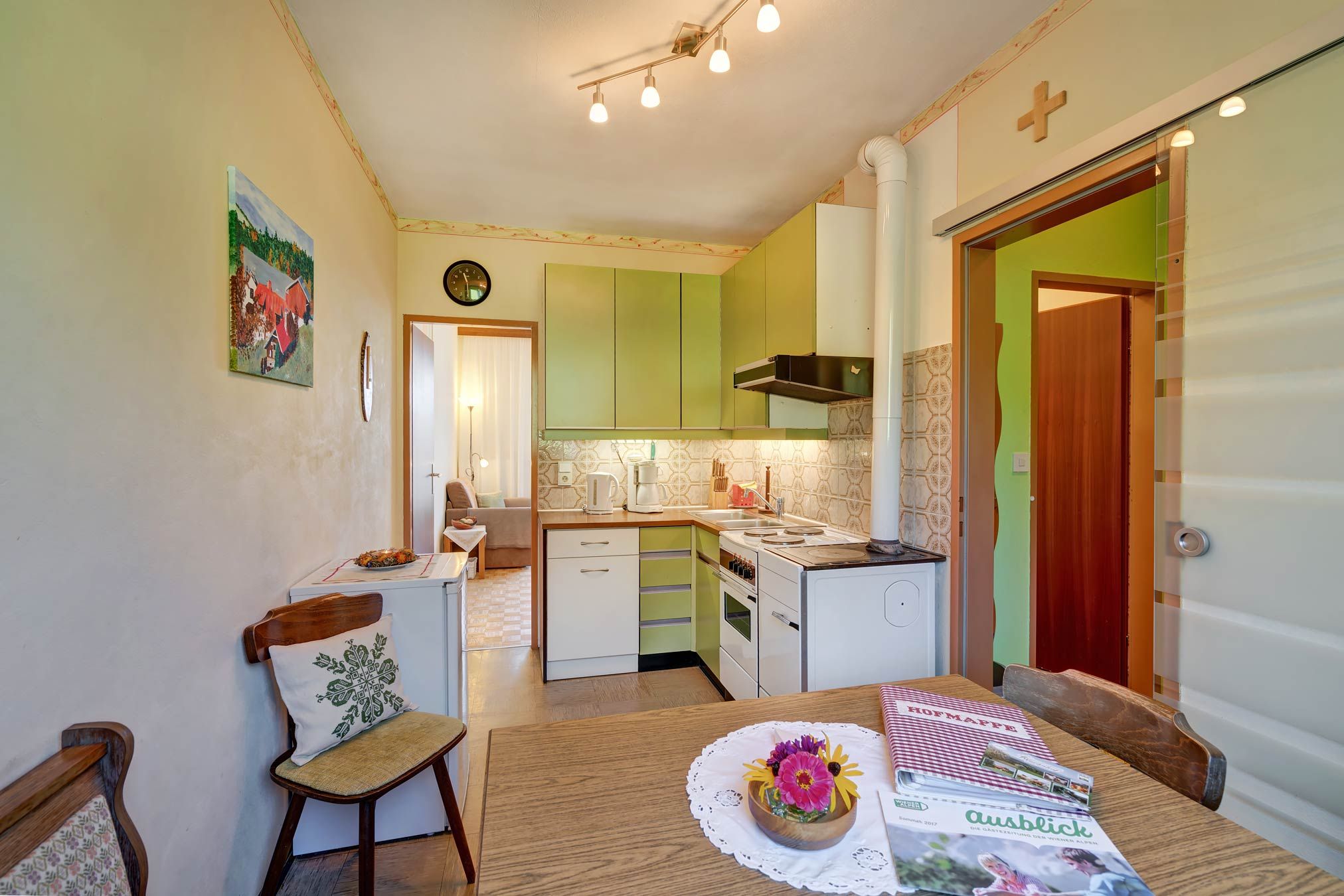Kitchen with green cupboards, dining table with flowers, door to the living room.