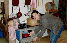 A woman and a child play in a historic kitchen with old kitchen utensils.