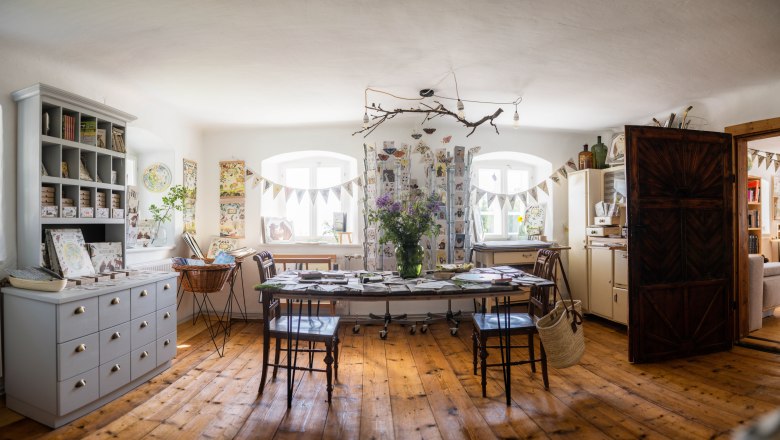 Interior view of a cozy studio with wooden floor, table and shelves full of artworks and decorations.