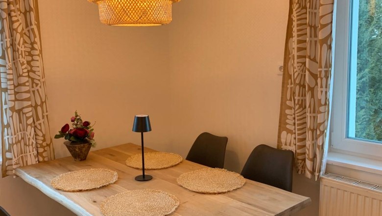 Dining area with wooden table, four black chairs, round lamp and window with curtains.