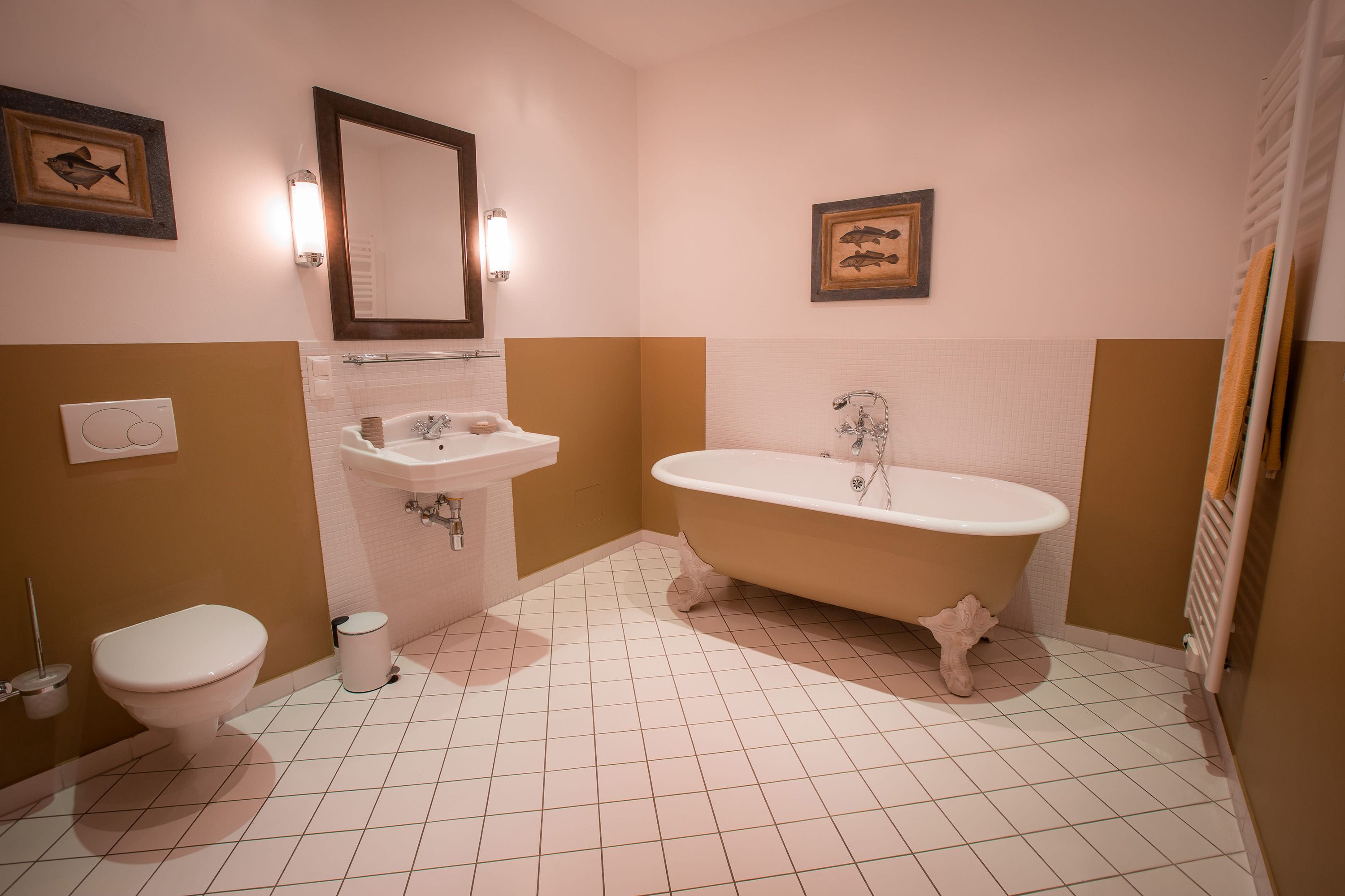 Elegant bathroom with free-standing bathtub, washbasin, mirror and WC. Walls in beige and white, decorated with fish pictures.