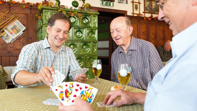 Three men playing cards in an inn with a green tiled stove in the background.