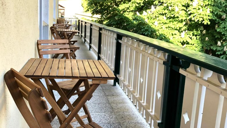 Wooden balcony with table and chairs, green trees next to it.