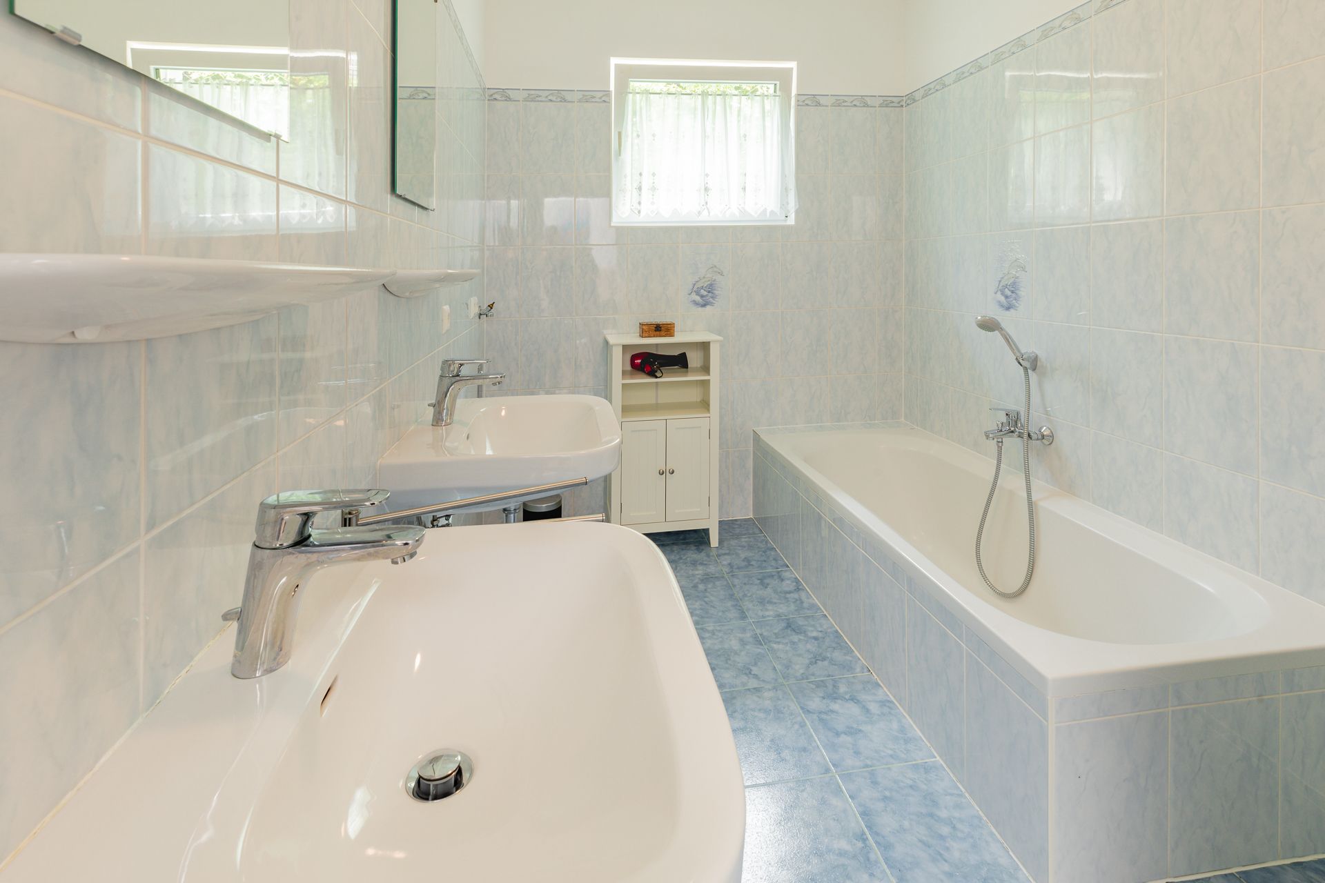 A bathroom with two washbasins, a bathtub and blue tiles.