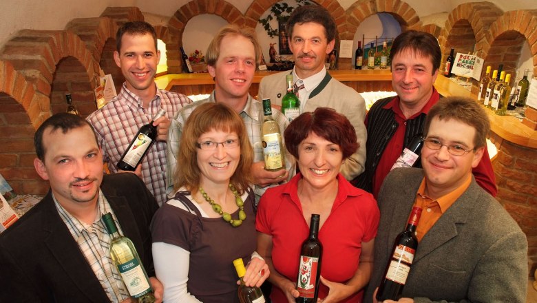 Group of people in a wine shop holding bottles of wine.