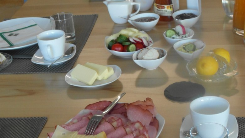 Breakfast table with cold cuts, cheese, bread rolls, vegetables and drinks.