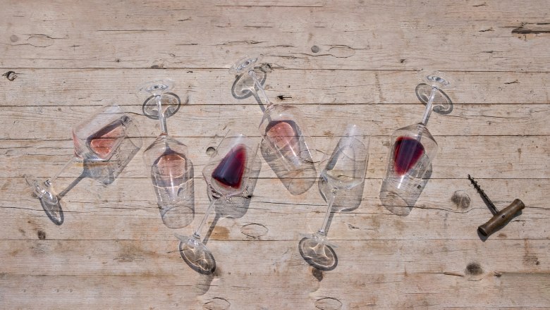 Six overturned wine glasses with red wine on a wooden table, a corkscrew next to them.
