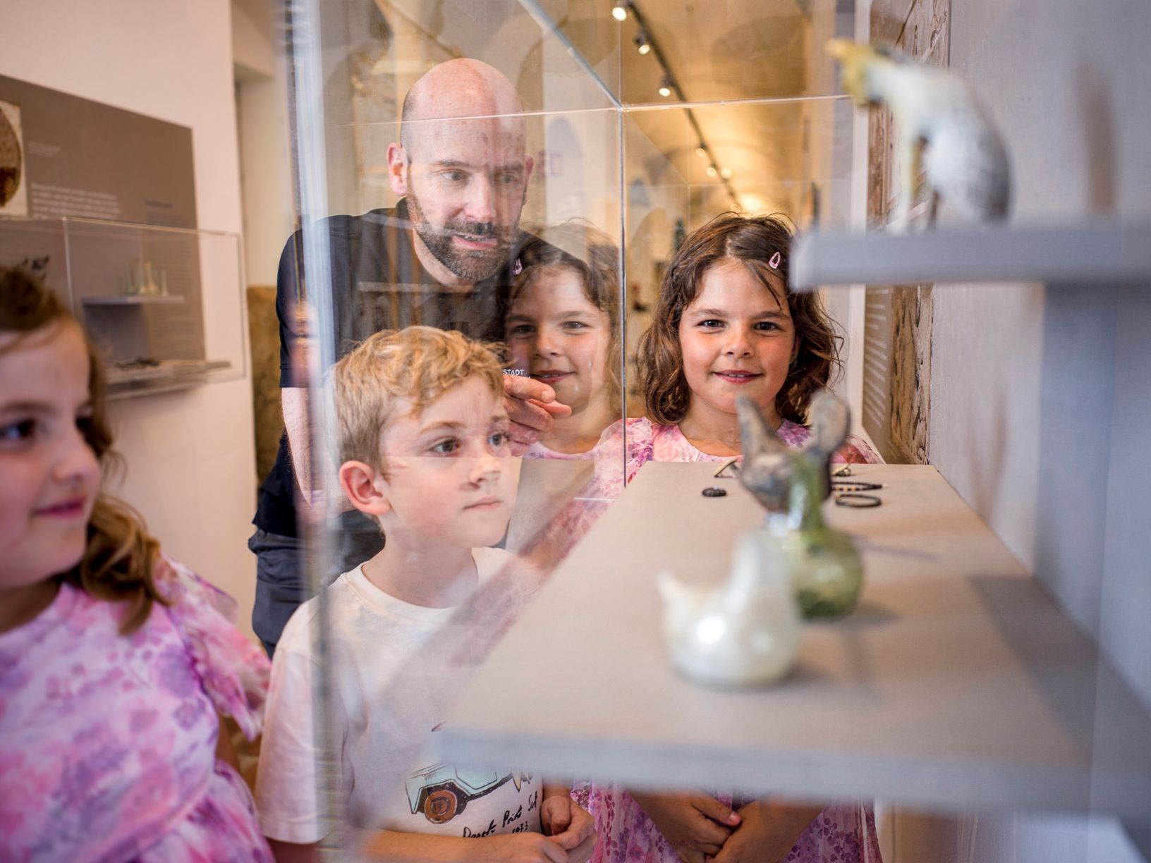 An adult shows children Roman jewelry in a glass display case