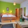 A cozy double room with green-painted wall, double bed, table, chairs and water bottle.