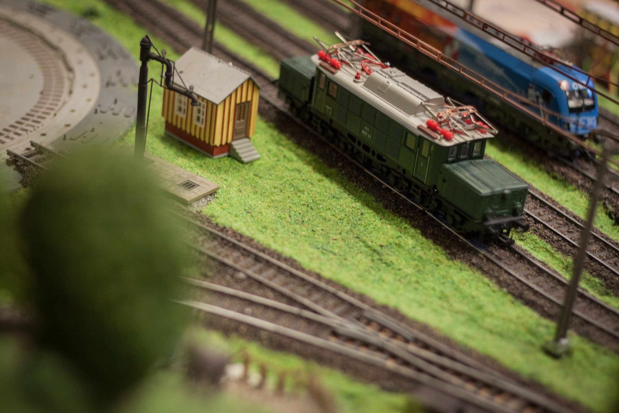 Model railroad with green train and small building on a layout.