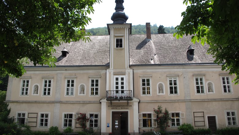 Exterior view of a historic building with a shingle roof and tower, surrounded by trees.