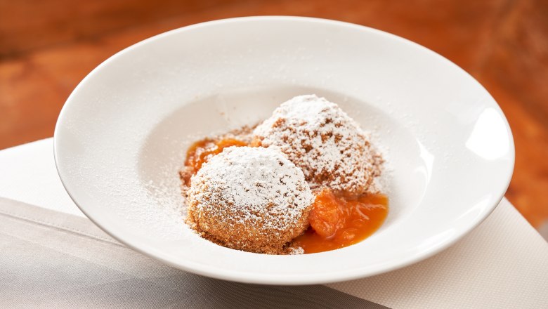 Two apricot dumplings with powdered sugar on a white plate.