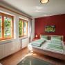 Bright bedroom with double bed, red walls and large windows with a view of the greenery.