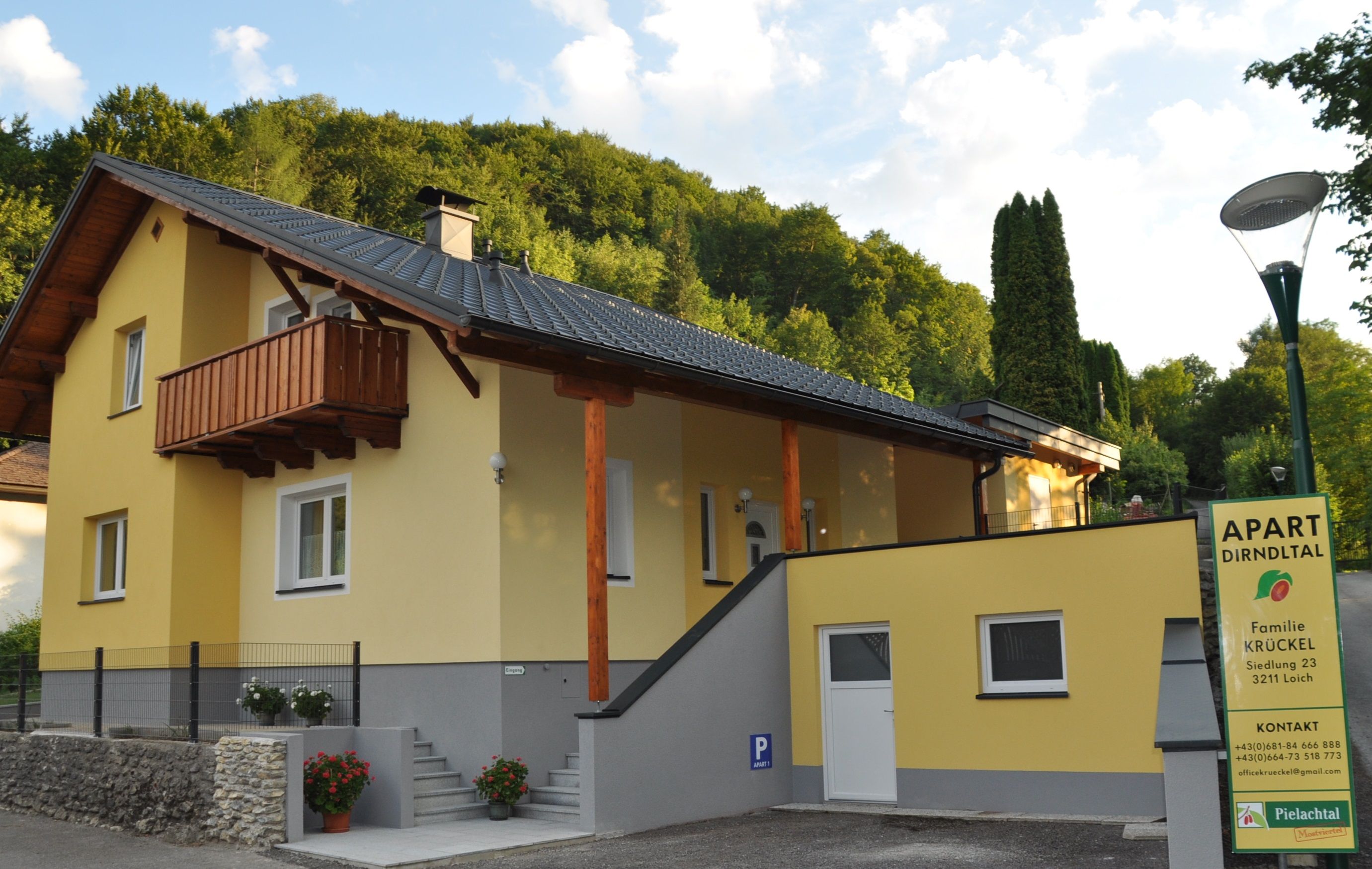 Yellow house with balcony and sign 'Apart Dirndltal' in front of a wooded hill.