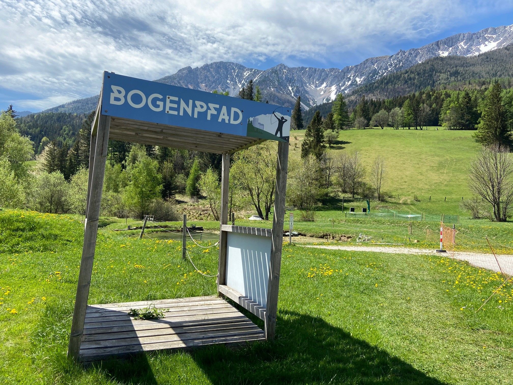 Wooden platform with sign 'Bogenpfad' in front of a mountain landscape.