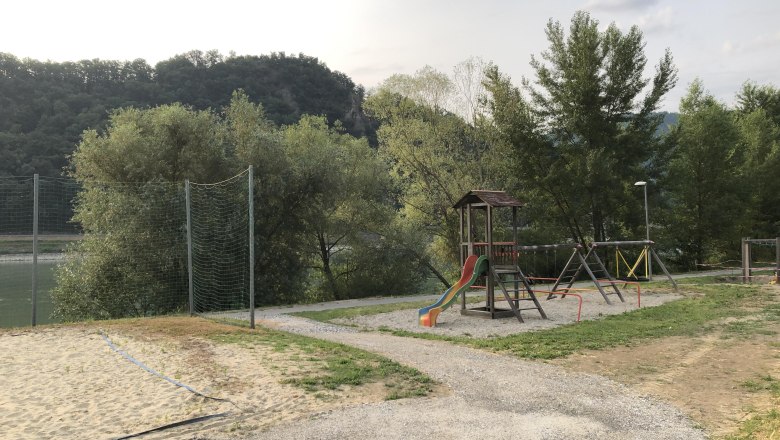 Playground with slide and swings, surrounded by trees and hills.