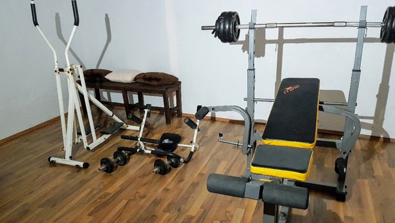 A fitness room with weight bench, cross trainer and dumbbells on a wooden floor.