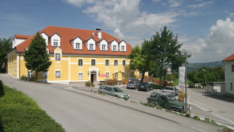 A yellow building with a red roof, surrounded by cars and trees, under a blue sky.