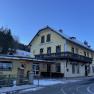Yellow building of the Karnerwirt inn with wooden balcony, surrounded by snow-covered trees.