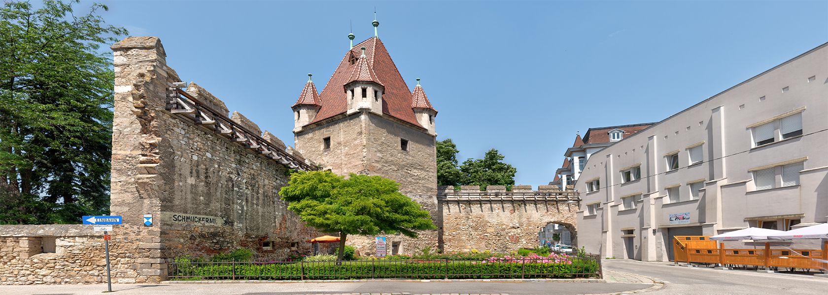 Historic stretching tower with red roof and adjoining city wall in an urban setting.