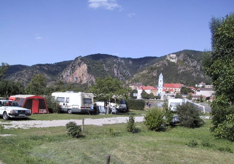 Campsite with caravans and tents in front of a mountain landscape and a church in the background.