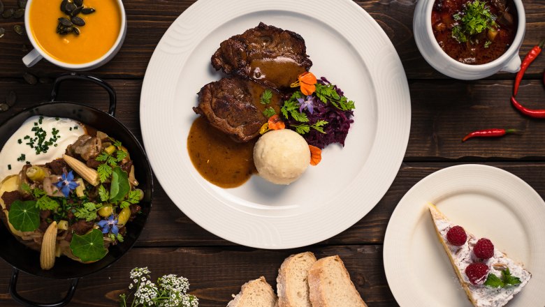 Various dishes on a wooden table, including soup, meat dish, stew, bread and cake.