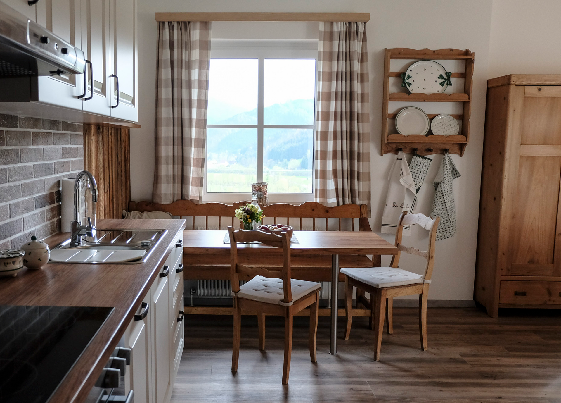 A cozy kitchen with wooden furniture and a view of the mountains through the window.