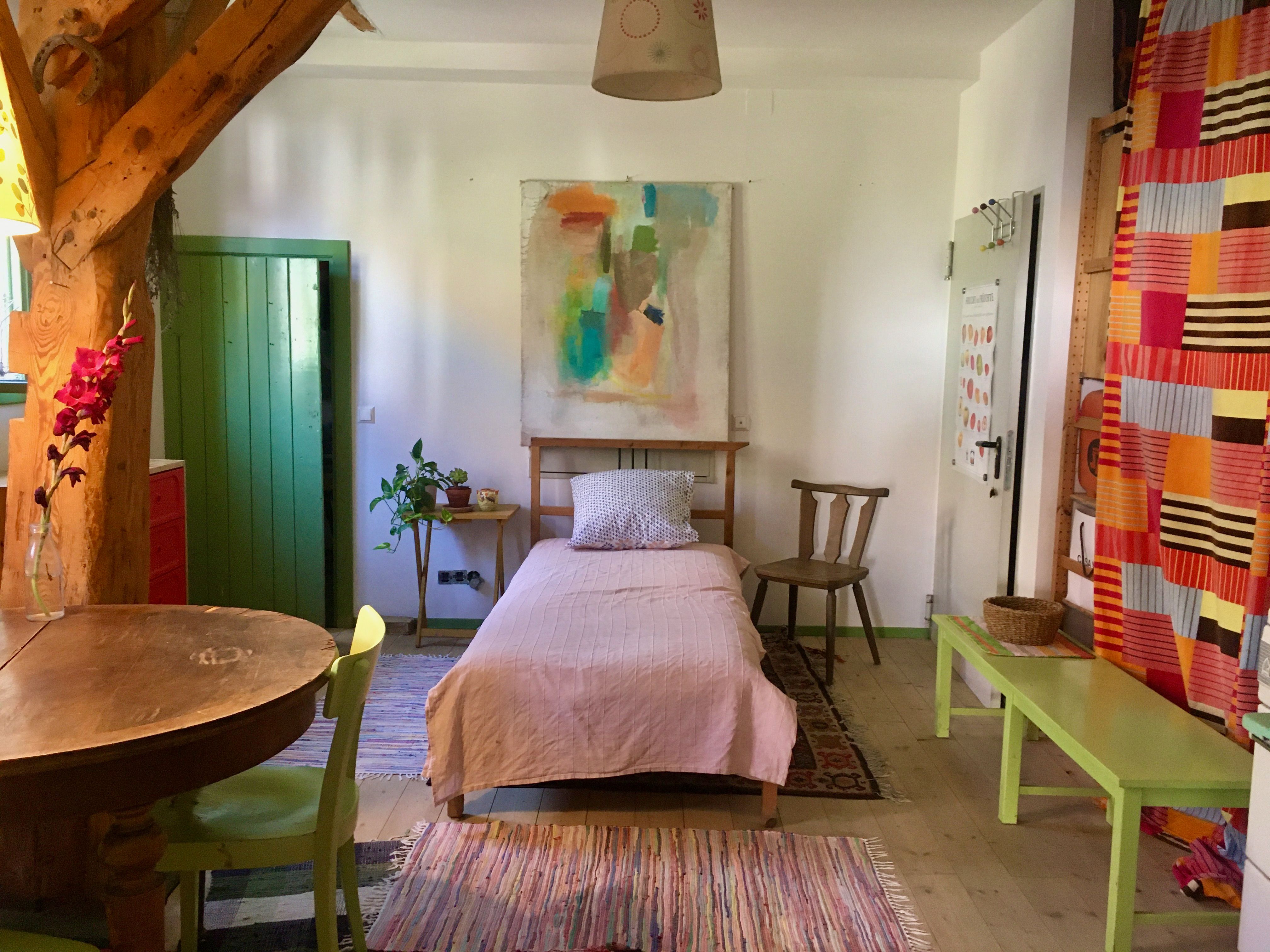 Single bed in a room with colorful furniture and a large painting above the bed.