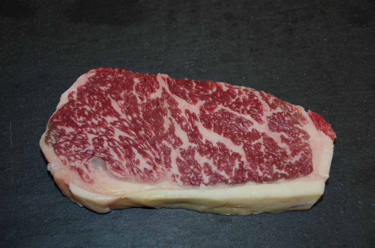 A piece of Wagyu beef with strong marbling on a black background.