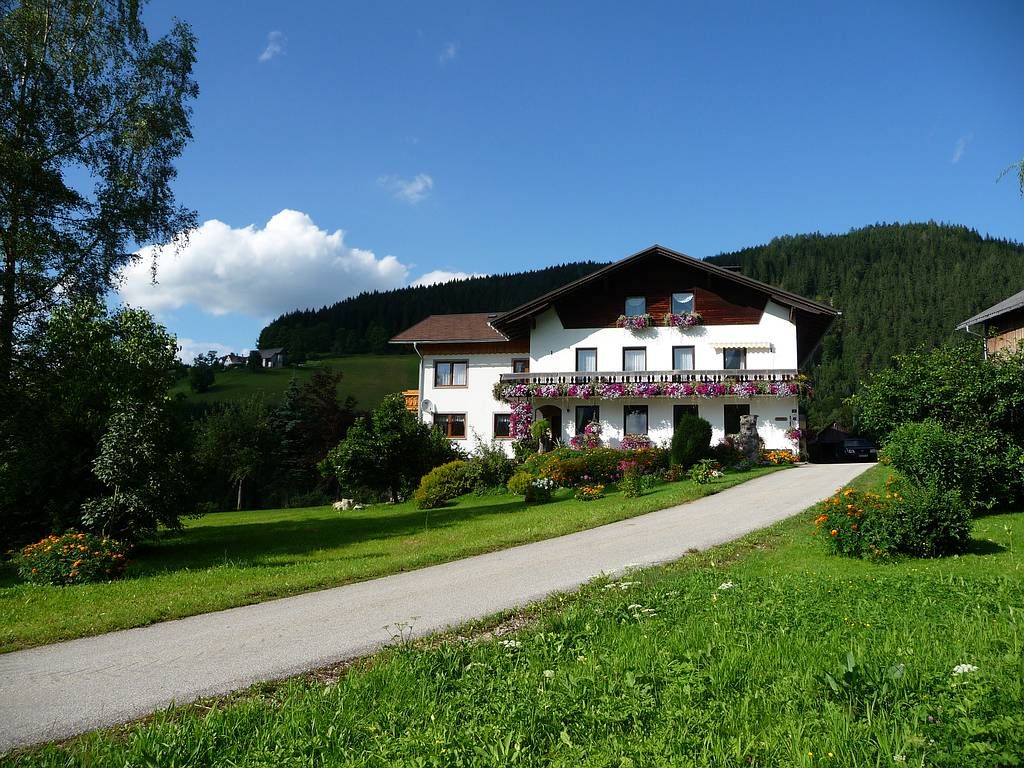 A farm with a house decorated with flowers in a green landscape under a blue sky.